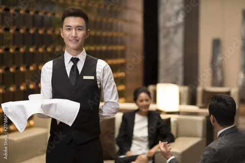 Cheerful young waiter serving coffee photo