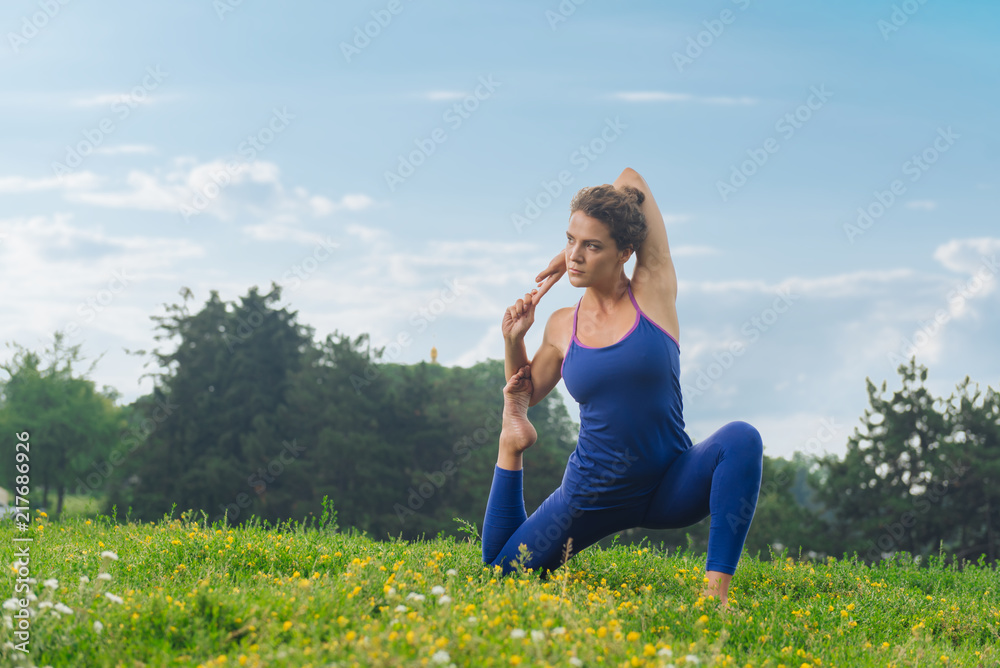 Stretching time. Slim beautiful woman feeling rested and contended while stretching sitting on green grass Stretching time. Slim beautiful woman feeling rested and contended while stretching sitting on green grass