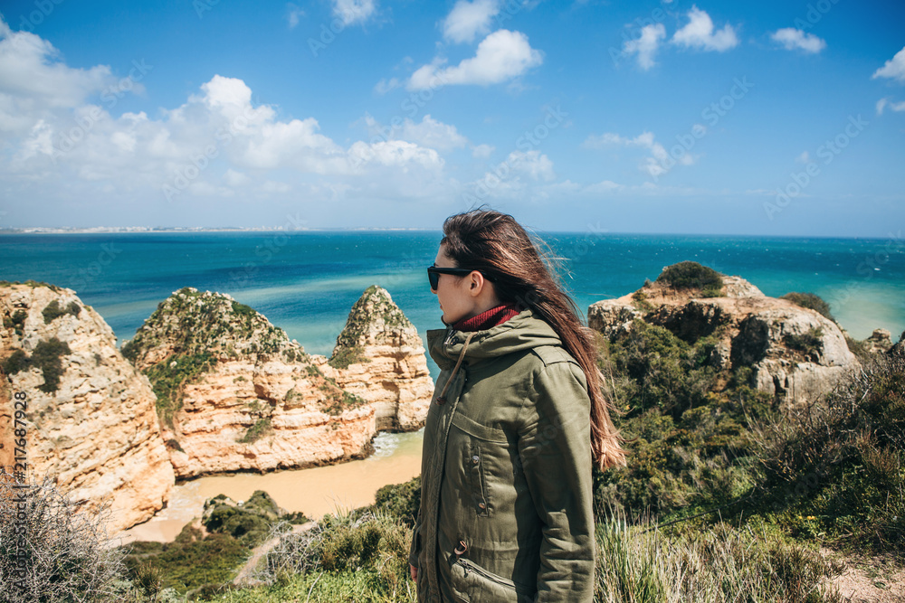 A young woman tourist enjoys the beautiful views of the Atlantic Ocean and the landscape off the coast in Portugal.