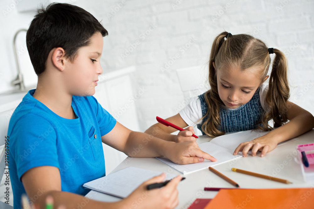 brother and sister doing homework together at table at home brother and sister doing homework together at table at home