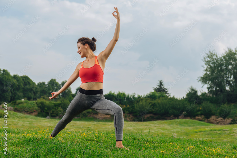 Favorite exercises. Dark-haired fitness trainer smiling while showing her favorite exercises standing on green grass Favorite exercises. Dark-haired fitness trainer smiling while showing her favorite exercises standing on green grass