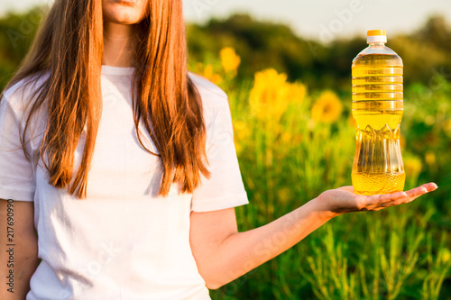 Young woman in white holding bottle of oil in sunflower field