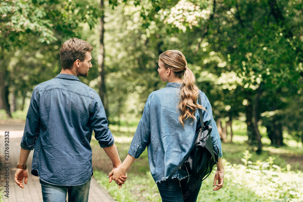 rear view of beautiful young couple in denim shirts walking by park