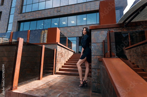 Young, beautiful girl on the background of an office building in a black dress.