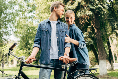 beautiful young couple with vintage bicycle standing at park