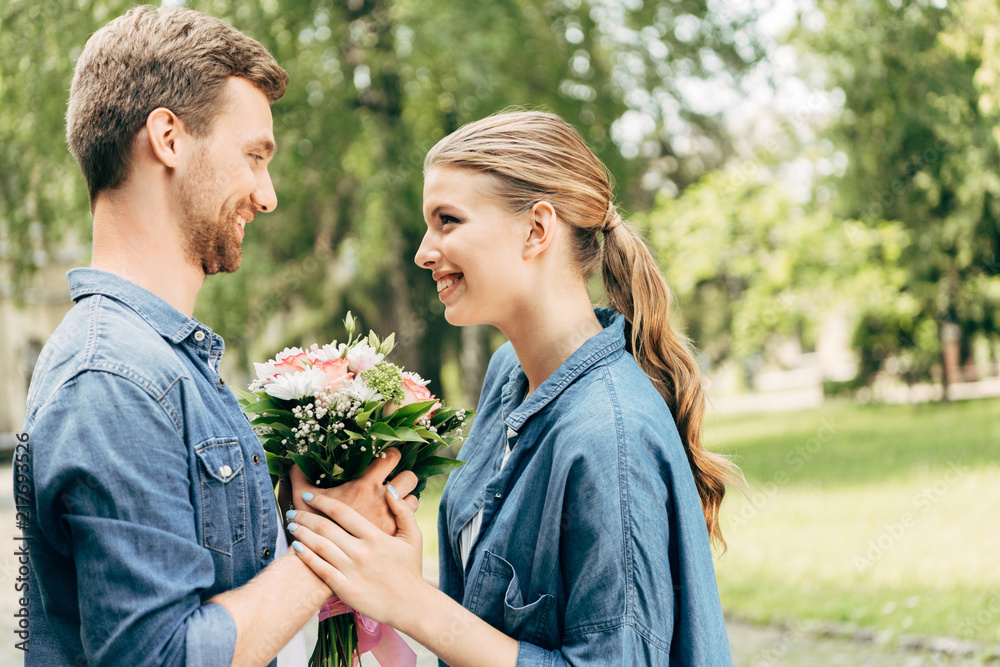 happy young couple holding flower bouquet at park and looking at each other happy young couple holding flower bouquet at park and looking at each other