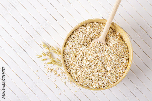 Oatmeal flakes in a wooden bowl on a white background. A wooden spoon in a bowl with porridge.