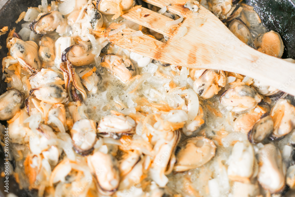 Fried mussels with onions, carrots and spices in a frying pan. Seafood dish.