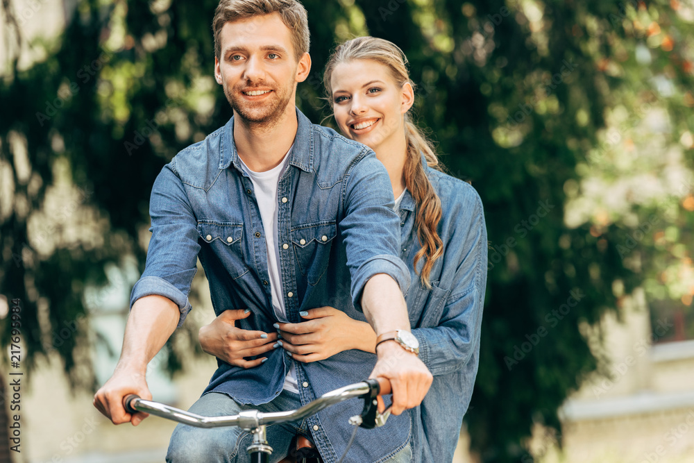 Fototapeta premium smiling young couple riding bicycle together at park