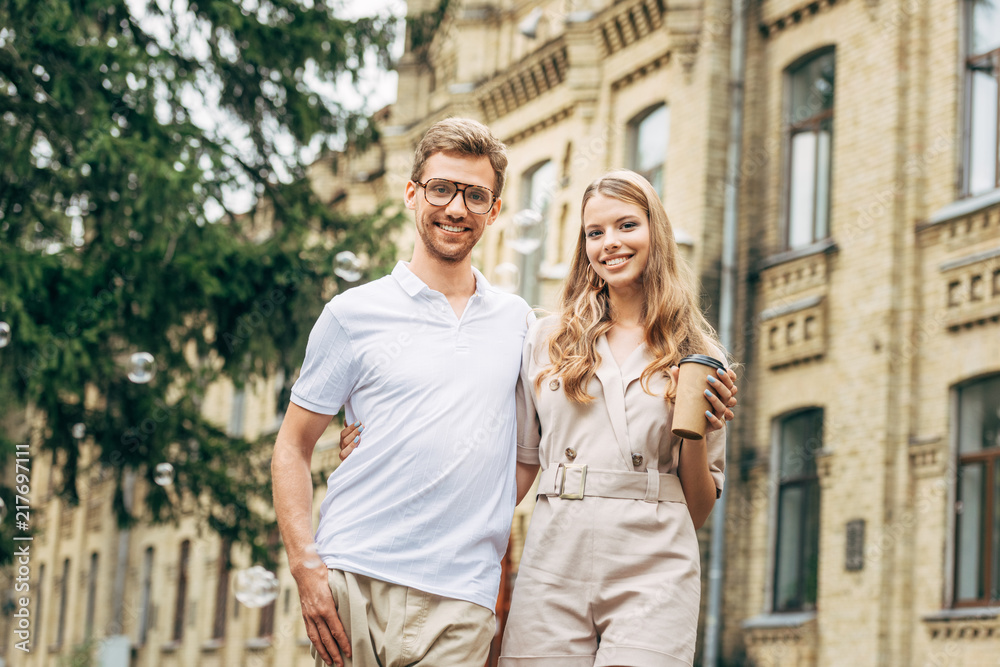 smiling young couple in stylish clothes looking at camera in front of old building