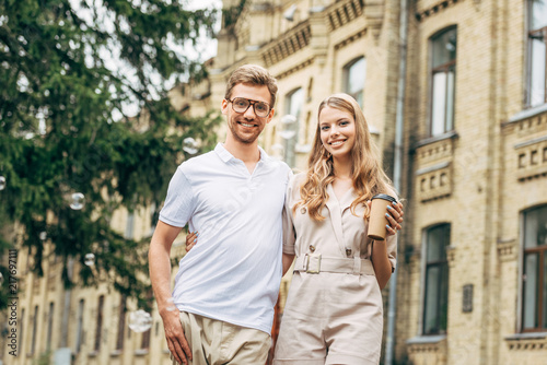 smiling young couple in stylish clothes looking at camera in front of old building
