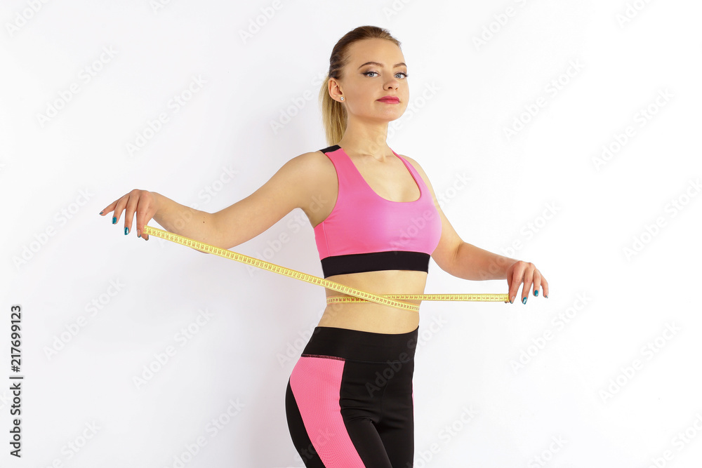 A sporty young girl measures a waist with a centimeter isolated on white background