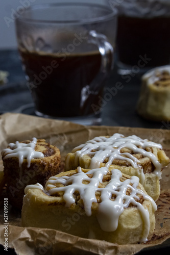Cinnamon rolls with white glaze icing on the top with the cup of coffee