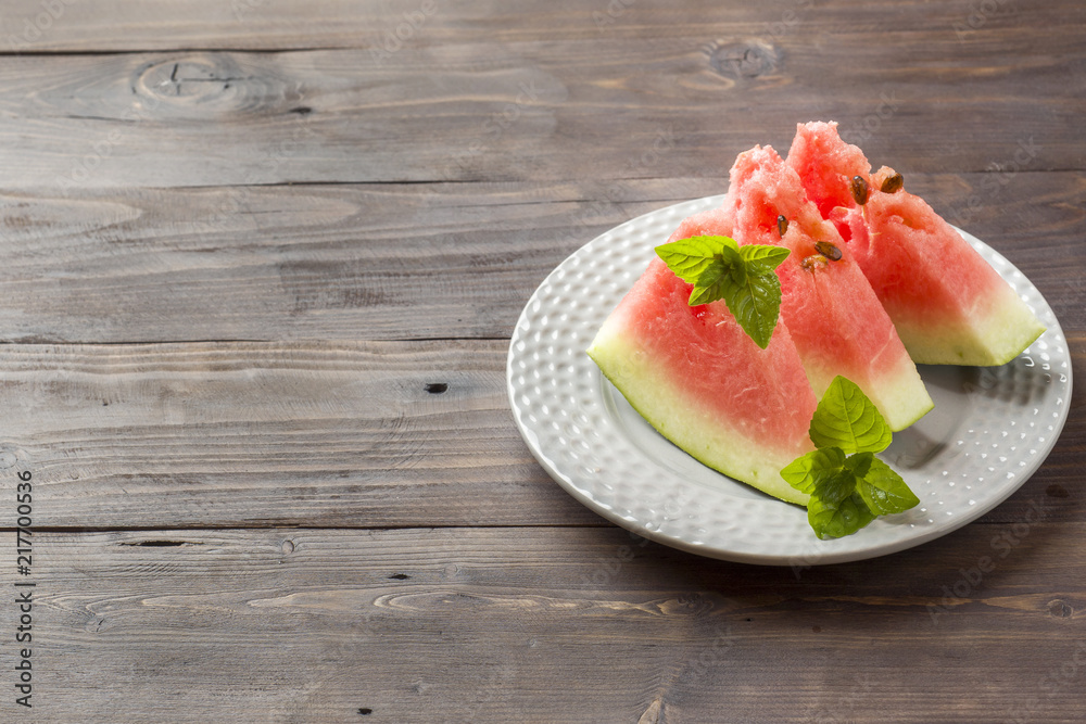 Watermelon sliced on a plate with mint leaves on a wooden background. Copy space Watermelon sliced on a plate with mint leaves on a wooden background. Copy space