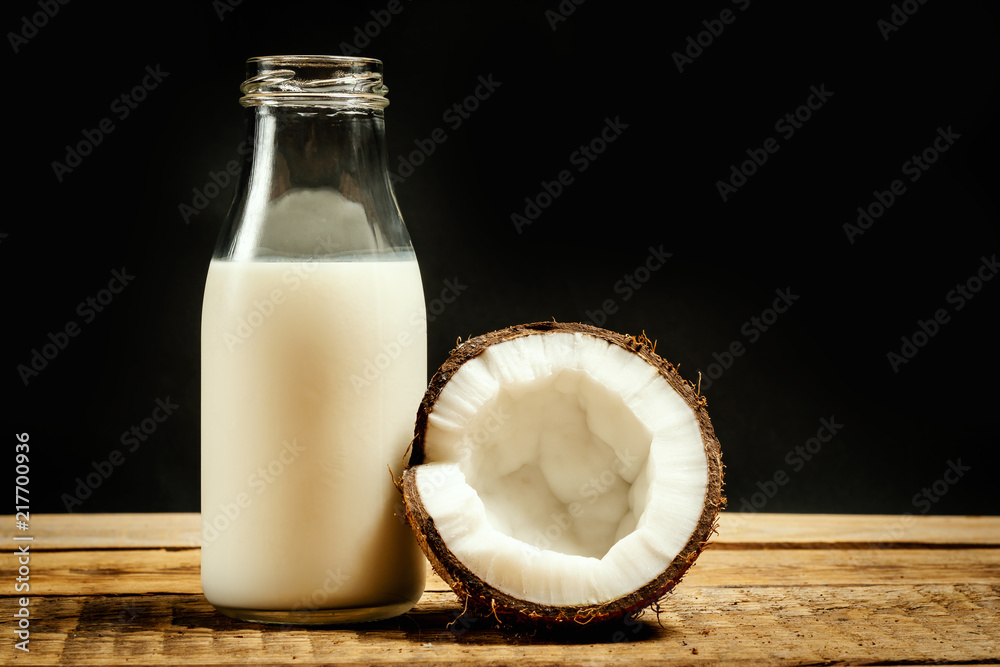 fresh brown coconuts and bottle of milk on a wooden table on a black background fresh brown coconuts and bottle of milk on a wooden table on a black background