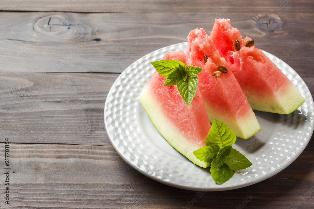 Watermelon sliced on a plate with mint leaves on a wooden background. Copy space Watermelon sliced on a plate with mint leaves on a wooden background. Copy space