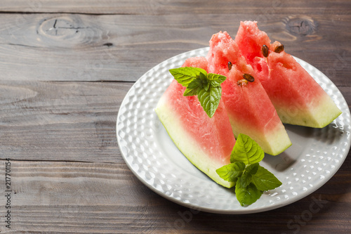 Watermelon sliced on a plate with mint leaves on a wooden background. Copy space