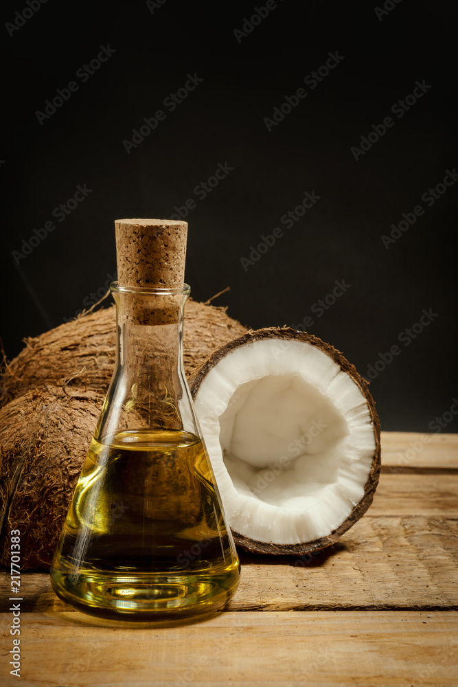 fresh brown coconuts and a bottle of oil on a wooden table on a black background fresh brown coconuts and a bottle of oil on a wooden table on a black background