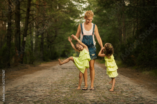 beautiful mother and two adorable daughters in dresses posing on the road in the summer forest
