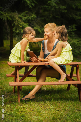 beautiful mother and two adorable daughters in dresses posing on a picnic table in a summer forest © superelaks