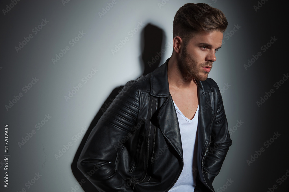 portrait of unshaved man in leather jacket leaning on wall