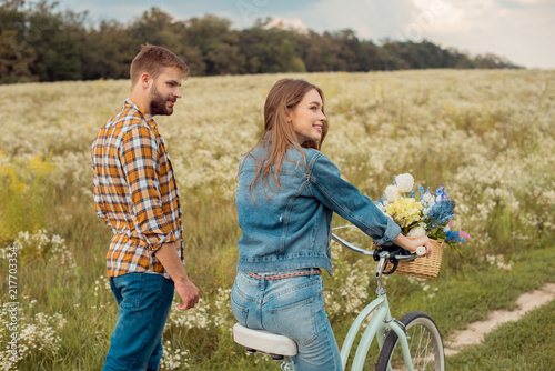 side view of young lovers with retro bicycle in field with wild flowers