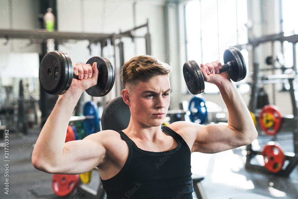 Young fit man in gym exercising with dumbbells. Young fit man in gym exercising with dumbbells.