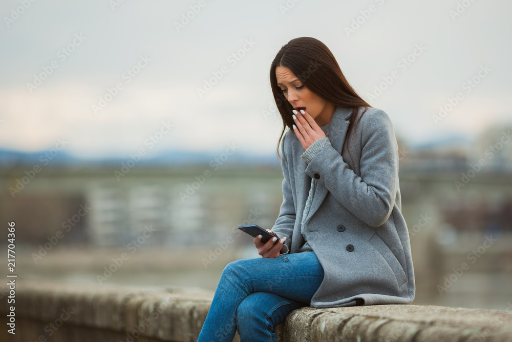 Young woman is surprised by message on the phone.