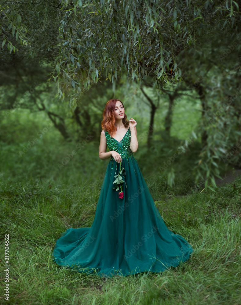 enigmatic girl in the clearing of grass is holding a rose in hands