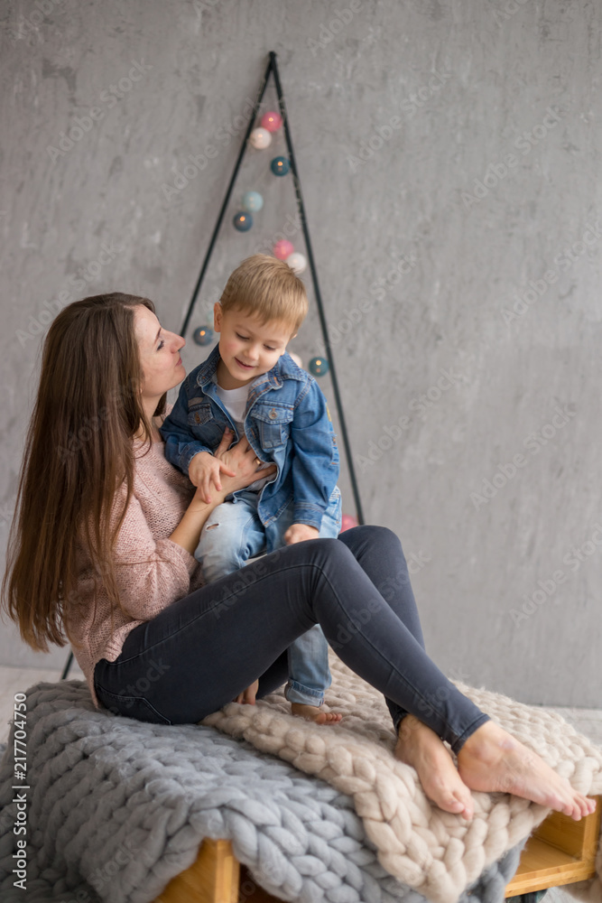 beautiful mother in a pastel t-shirt is having fun with her little son on the background of a new-year decor, garlands. beautiful mother in a pastel t-shirt is having fun with her little son on the background of a new-year decor, garlands.