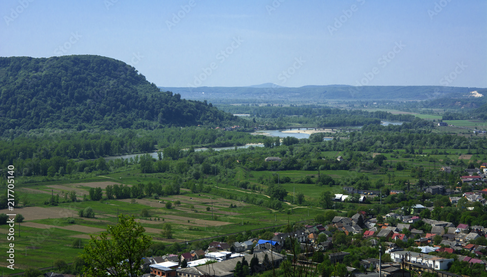 Fototapeta premium Colorful exalted view from a bird's eye view to houses in residential district in the city of Khust, Western Ukraine with high mountains in the background on a background of green vegetation.