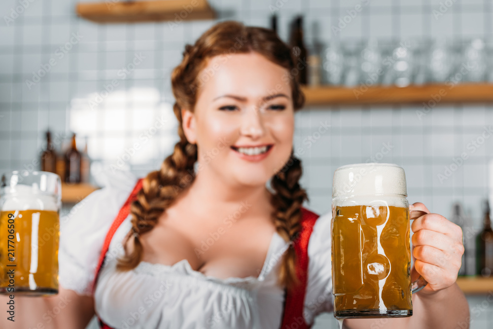 selective focus of oktoberfest waitress in traditional bavarian dress showing mugs of light beer near bar counter selective focus of oktoberfest waitress in traditional bavarian dress showing mugs of light beer near bar counter