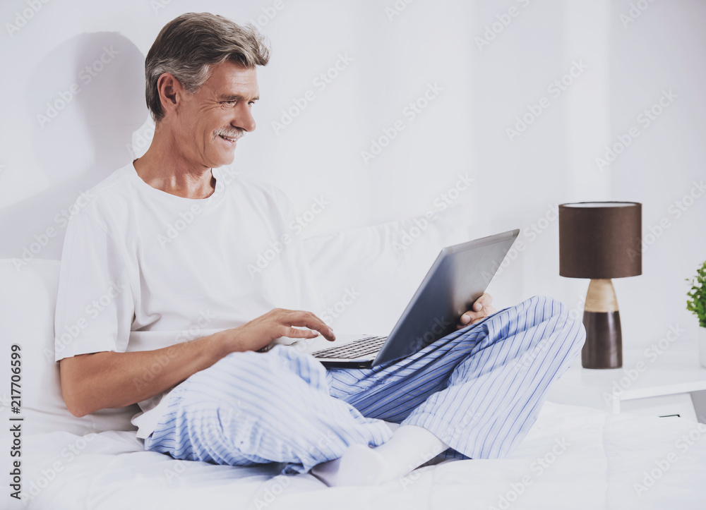 Old Man Using Laptop while Sitting in Bed. Old Man Using Laptop while Sitting in Bed.