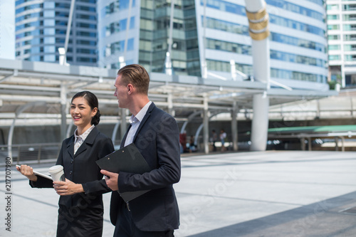 Asian businesswoman and Caucasian businessman walking together in the city and talk about business plan.