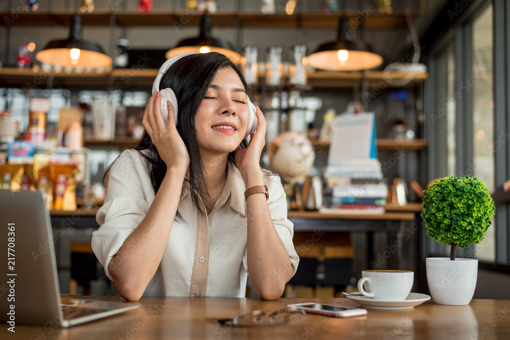 Happy Asian woman relaxing and listening music in coffee shop with computer laptop and coffee cup. People and lifestyles concept. Freelance and outdoors workplace outdoors theme.