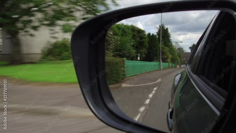 Reflection in a car wing mirror of a drive along a village road. Reflection in a car wing mirror of a drive along a village road.