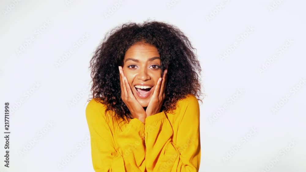 Beautiful african american woman with afro hair in yellow wear smiling, pleasantly surprised to camera over white wall background. Cute mixed race girl's portrait with amazement Beautiful african american woman with afro hair in yellow wear smiling, pleasantly surprised to camera over white wall background. Cute mixed race girl's portrait with amazement