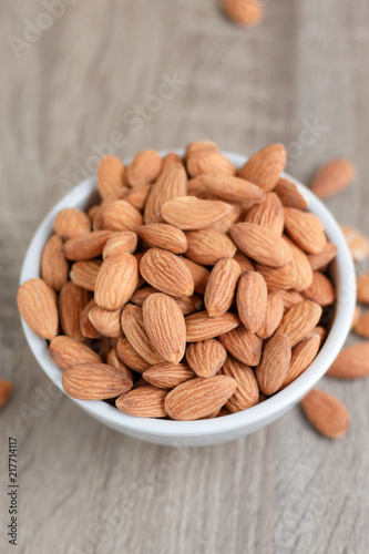 Pile of almonds nut in a while bowl against wooden background select focus shallow depth of field