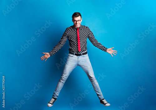 Portrait of a young man with glasses in a studio on a blue background, jumping.