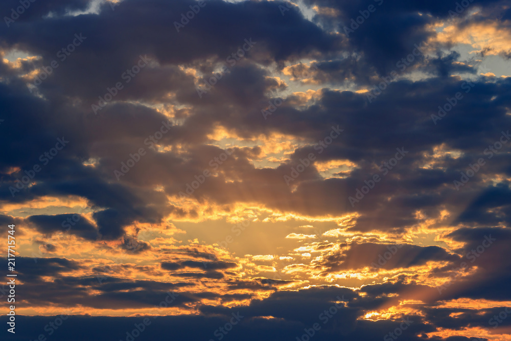 Sky with dark clouds and orange rays of the sun at sunset
