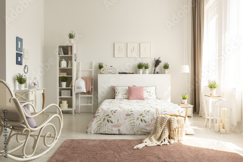 White bedroom interior with dirty pink carpet, rocking chair, window with drapes and king-size bed in the real photo photo