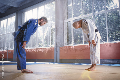 Fototapeta Two judo fighters or athletes greeting each other in a bow before practicing martial arts in a fight club. The two fit men in uniform. Fight, karate, training, arts, athlete, competition concept