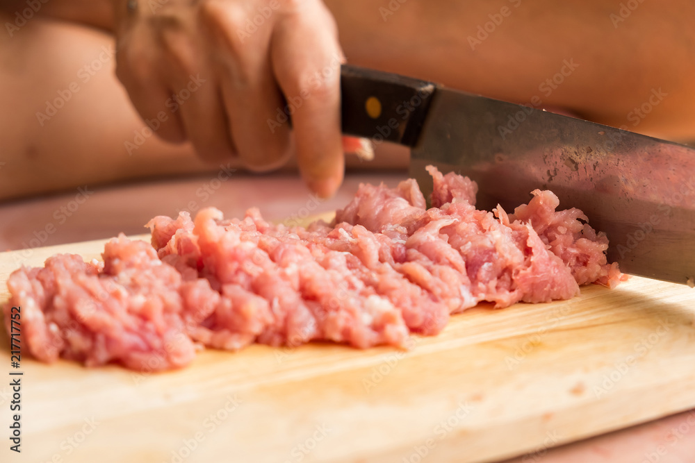 Chef is chopping the raw pork on the wooden cutting board with a sharp knife to cook in the kitchen.
