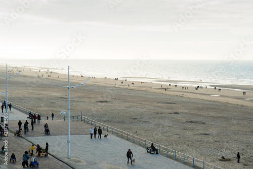 people strolling on the sea-wall at the North Sea at fall, other are playing with there childeren on the beach photo