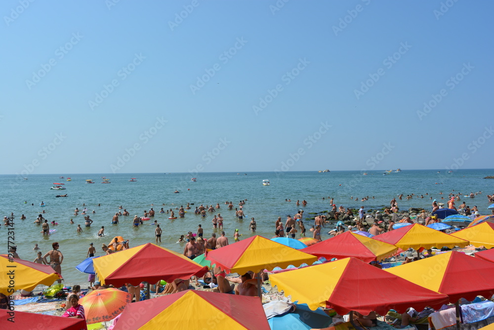 Bright red yellow beach umbrellas on the Black Sea coast with tourists and vacationers