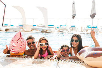 Happy family with children wearing sunglasses swimming in pool, with rubber ring during travel or vacation
