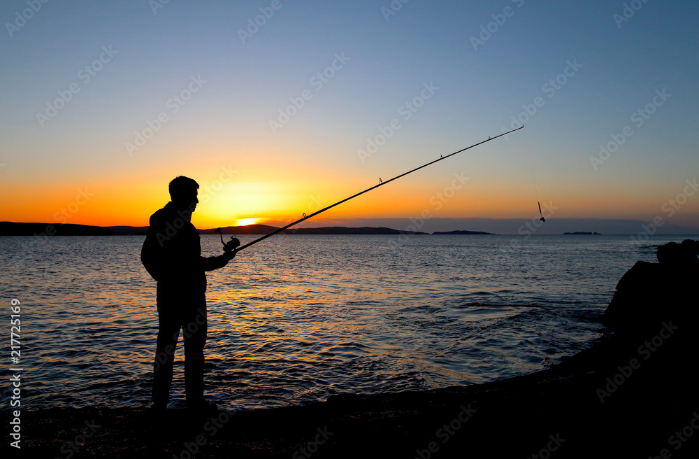 Boy rock fishing in colourful sunset on coast line