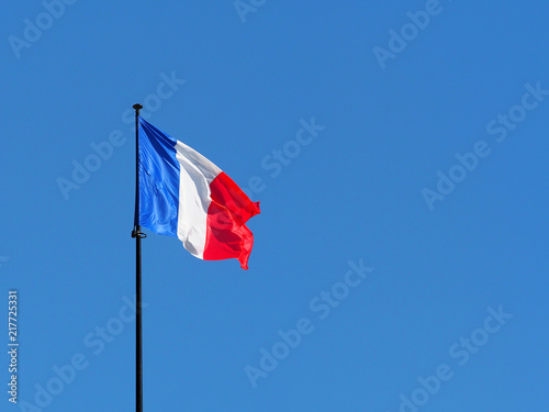 Flag of France on flagpole against the clear blue sky. Space for text