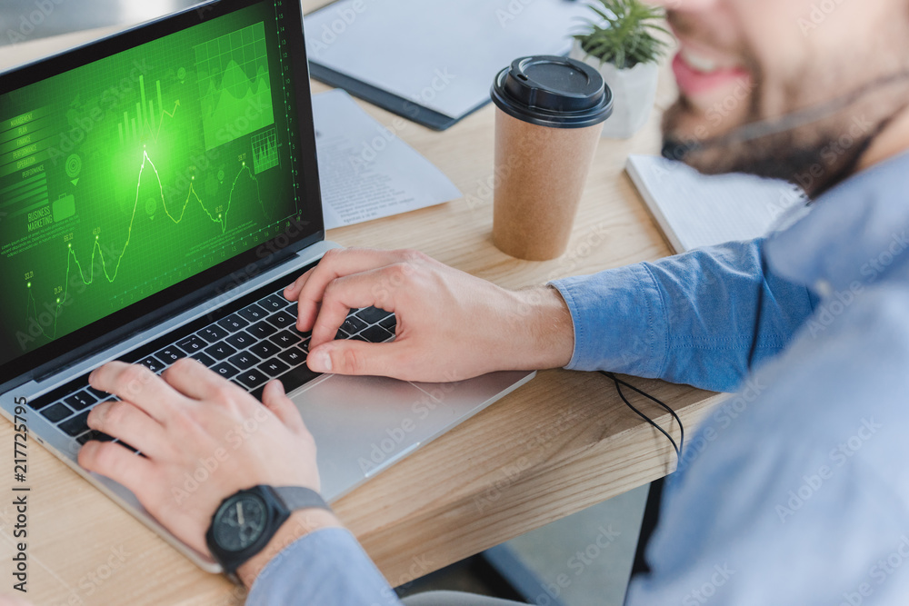 selective focus of smiling businessman in headset using laptop with business charts on screen