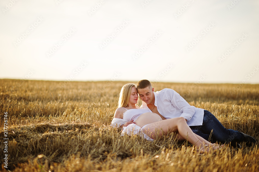 Pregnant couple in wreath field at white underwear clothes on sunset. Happy moments of pregnancy. Pregnant couple in wreath field at white underwear clothes on sunset. Happy moments of pregnancy.